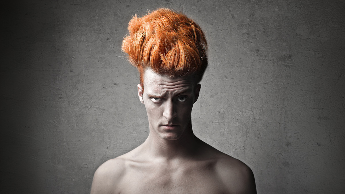 A pale, ginger man on a dark background with a great head of thick hair